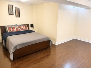 Quarto com cama, soalho de madeira, prateleira na parede e duas imagens emolduradas.