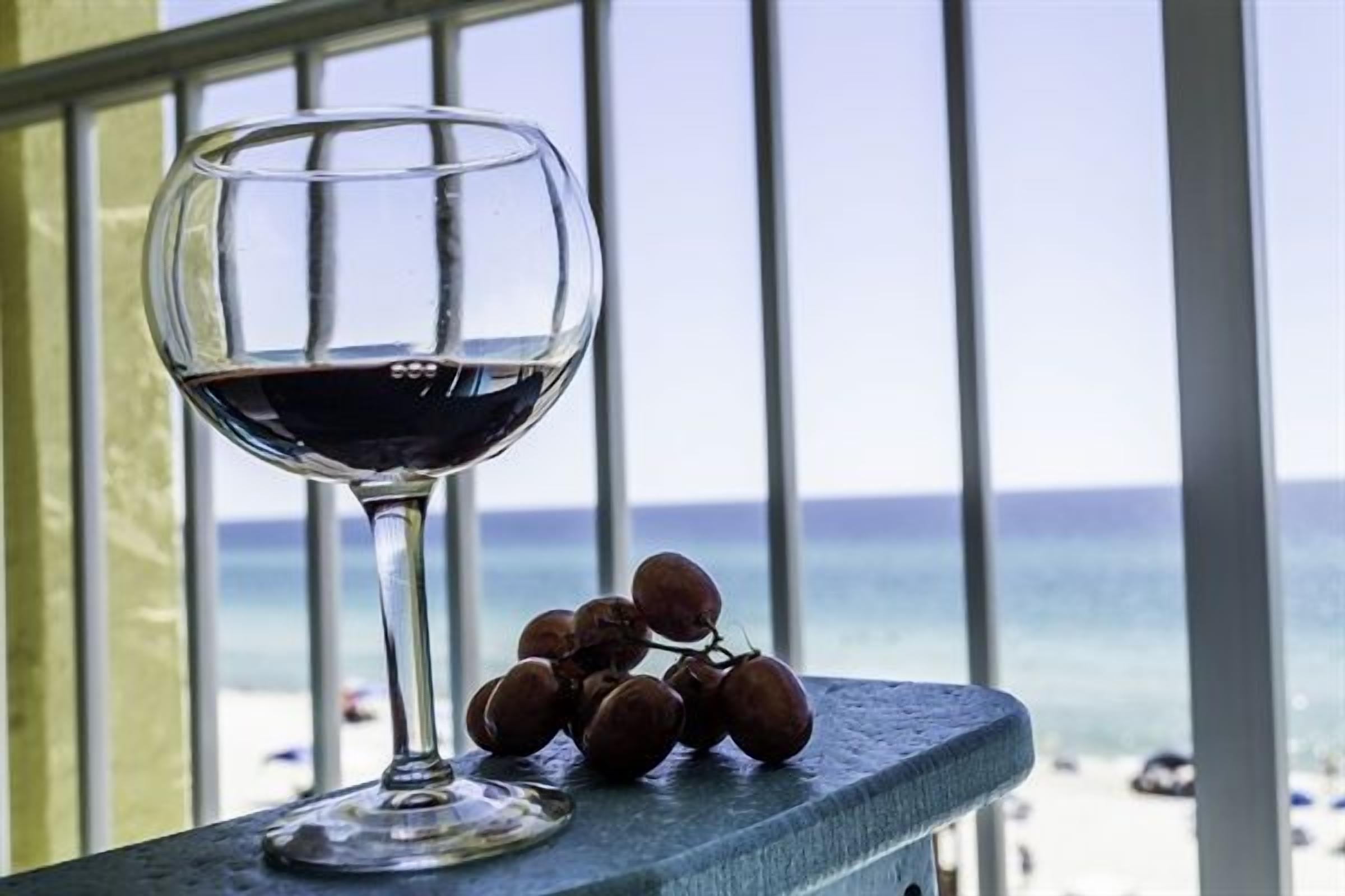 A glass of red wine on a balcony with a view of the ocean.