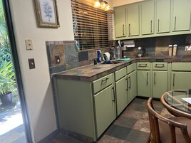 A kitchen with green cabinets, a stone backsplash, and a window with blinds.