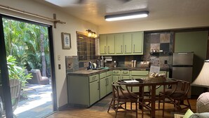 A kitchen with green cabinets, a dining table with wicker chairs, and a refrigerator. - Mango Suite (Kihei)