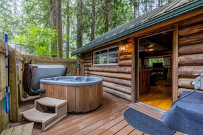 A log cabin with a hot tub, wooden deck, and a rustic interior.