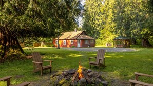 Een blokhut met een vuurkuil, omringd door Adirondack stoelen, gelegen in een bebost gebied met een tuinpaviljoen en picknicktafels.