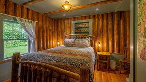 Een kamer met houten lambrisering, een bed, een tafeltje en een stoel.