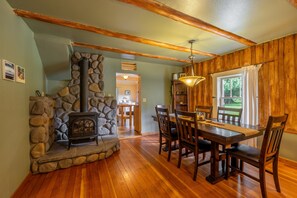 Un espace repas agrémenté d’une cheminée en pierre, de poutres en bois et offrant une vue sur l’extérieur.