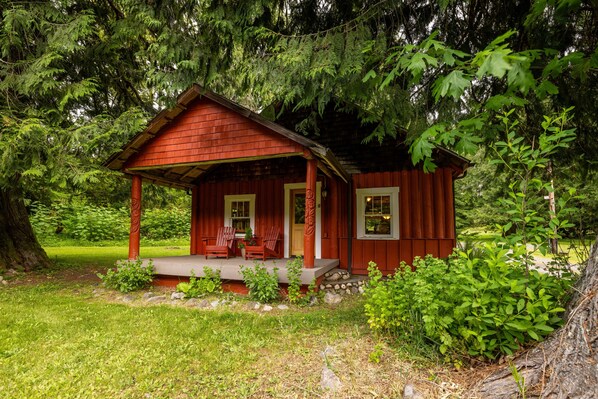 Une petite cabane rustique dotée d’un porche, entourée d’une végétation luxuriante.