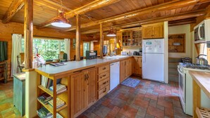 Interior de una cabaña de madera con cocina, armarios de madera, un refrigerador blanco, una estufa y un ventanal grande.