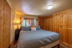 A bedroom with a bed, wooden walls, a nightstand, a lamp, and a window with curtains.