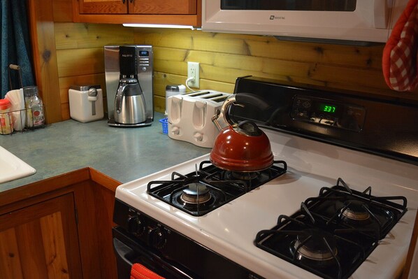 A kitchen with a stove, toaster, coffee maker, and microwave.