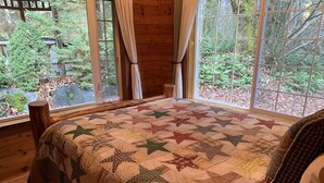 Um quarto aconchegante com uma cama grande, paredes de madeira e uma janela com vista para uma área arborizada.