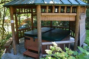 Un pabellón de madera con un jacuzzi, un banco de madera y una mesa de picnic.