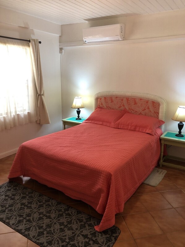 Une chambre à coucher avec un lit, deux tables de chevet avec des lampes, une fenêtre avec des rideaux et un appareil de climatisation fixé au mur.