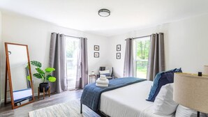 Una habitación de hotel moderna con cama, mesita de noche, lámpara y vistas al exterior.