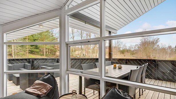 A sunlit outdoor seating area with wicker furniture and a wooden table, overlooking a natural landscape. - Stunning home in Ebeltoft with kitchen (Ebeltoft)