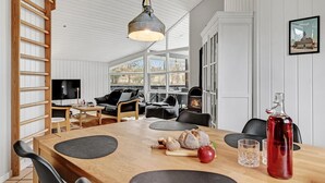 A modern living room with a wooden dining table, black leather sofa, and a fireplace. - Stunning home in Ebeltoft with kitchen (Ebeltoft)