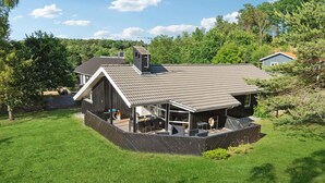 A modern house with a large deck, surrounded by a well-maintained lawn and dense trees. - Stunning home in Ebeltoft with kitchen (Ebeltoft)