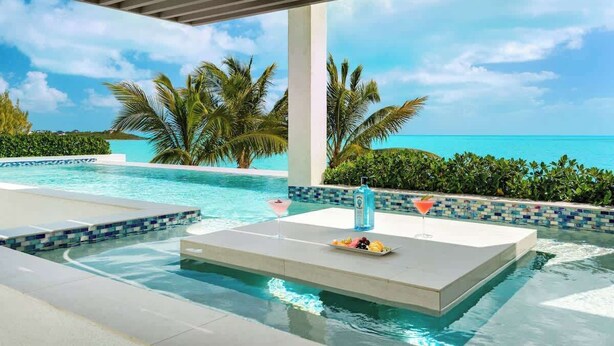 Ein Poolbereich mit Blick auf das Meer, eine Bar mit einem Getränk und eine Liege.