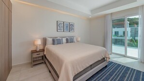 A modern bedroom with a large bed, a nightstand with a lamp, and a view of a balcony through a glass door. - Mantaray Villa #6 Sum (roatan)