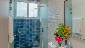 A modern bathroom with a glass-enclosed shower, a white toilet, a sink with a mirror, and a window providing natural light. - Mantaray Villa #6 Sum (roatan)