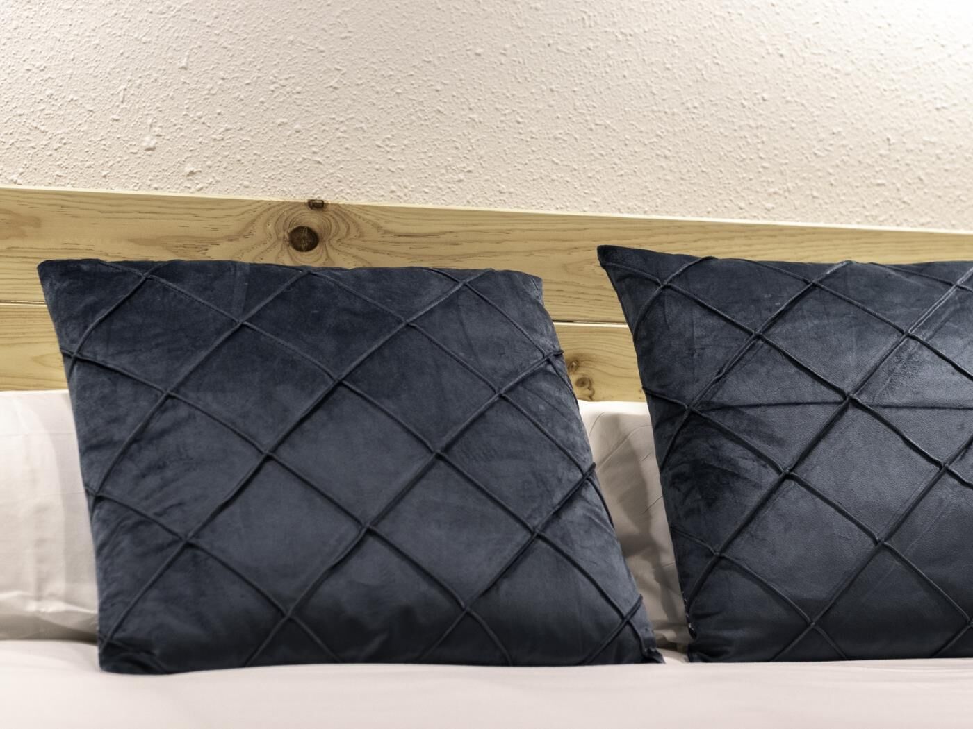 Una cama con cabecera de madera y dos almohadas acolchadas azul oscuro.
