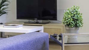 A modern living room with a flat-screen TV, a potted plant, and a glass coffee table.