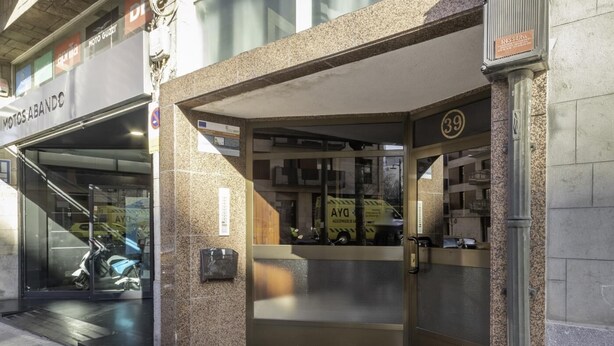 A building entrance with a glass door, a small outdoor seating area, and a visible sign for 'Motos Abando'.