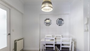 A dining area with a white table and chairs, a hanging light fixture, and two wall-mounted mirrors.