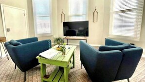 A living room with two blue armchairs, a green coffee table, and a flat-screen TV on a stand. - Completely remodeled efficiency unit one block from the Smithville square (Smithville)