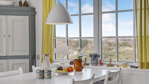 A dining area with a white table, chairs, and a window with yellow curtains.