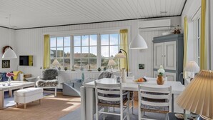 A bright, spacious room with a large window, white furniture, and a dining table.