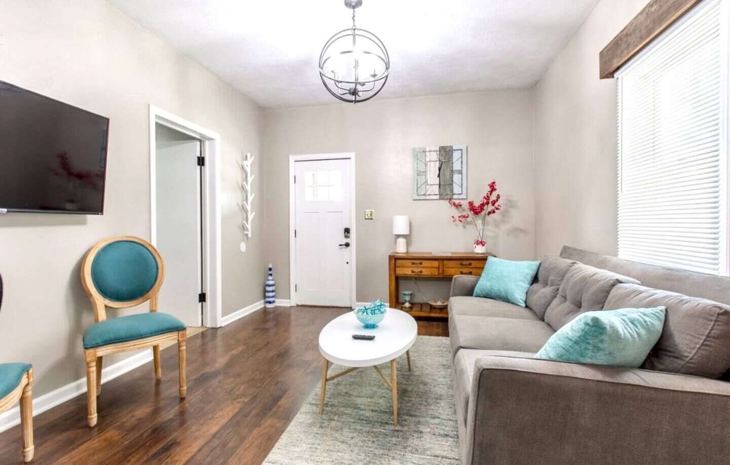 A living room with a sofa, a chair, a coffee table, and a TV on the wall.