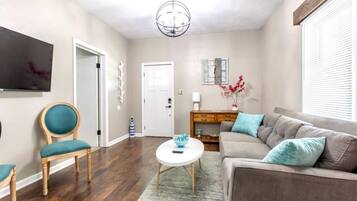 A living room with a sofa, a chair, a coffee table, and a TV on the wall.