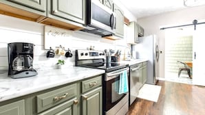 A kitchen with green cabinets, a black stove, a coffee maker, and a hanging pot rack. - Modern and comfy home five minutes from downtown (Hannibal)