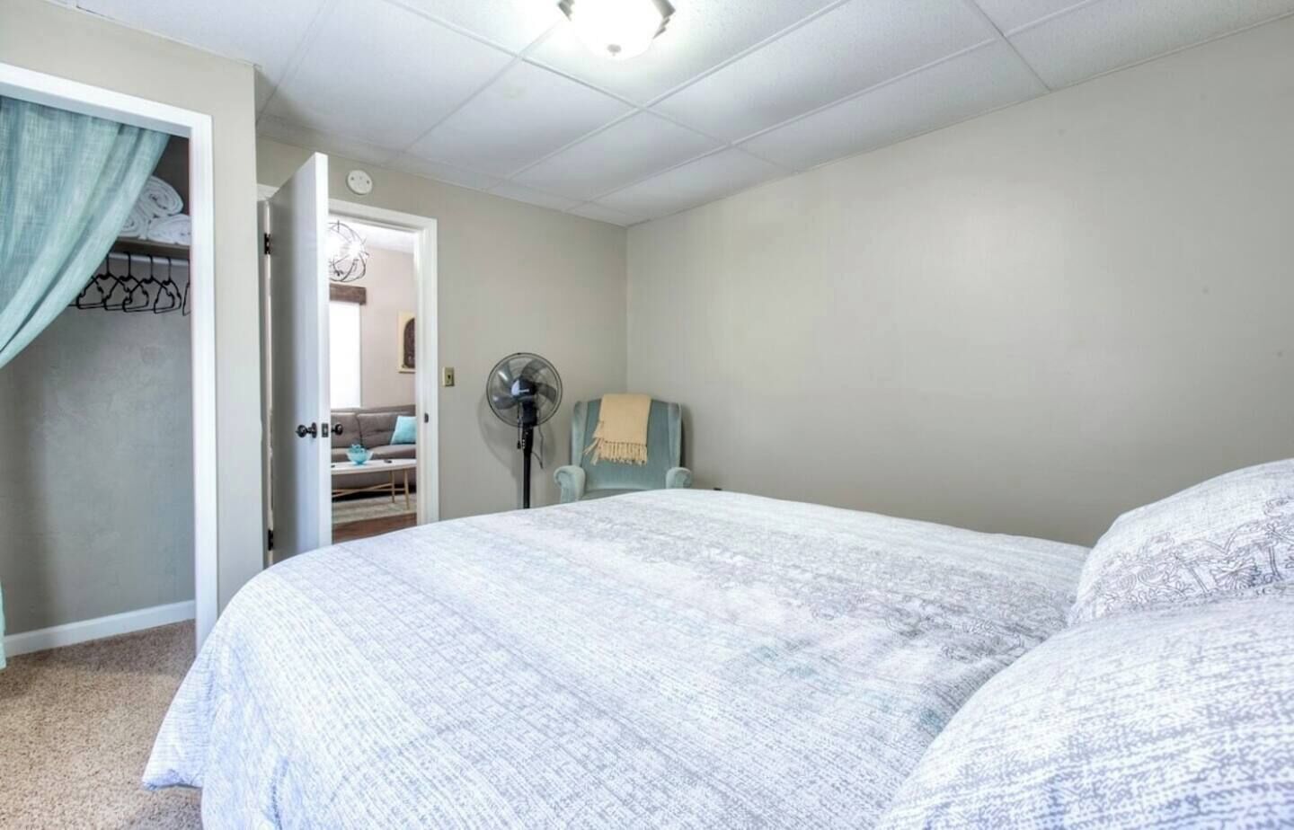 Una camera da letto con un letto, una ventola da terra e una porta che dà su un'altra stanza.