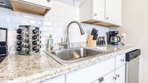 A kitchen with white cabinets, a stainless steel sink, a coffee maker, and a spice rack. - Great for a staycation, or work-from-home alternative (Kansas City)