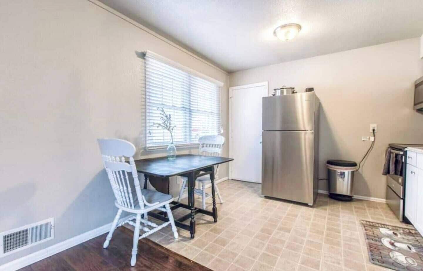 A compact kitchen with a dining table, chairs, a refrigerator, and a trash can.