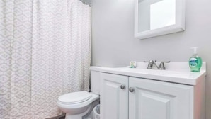 Un baño con inodoro, lavamanos con espejo y cortina de ducha.