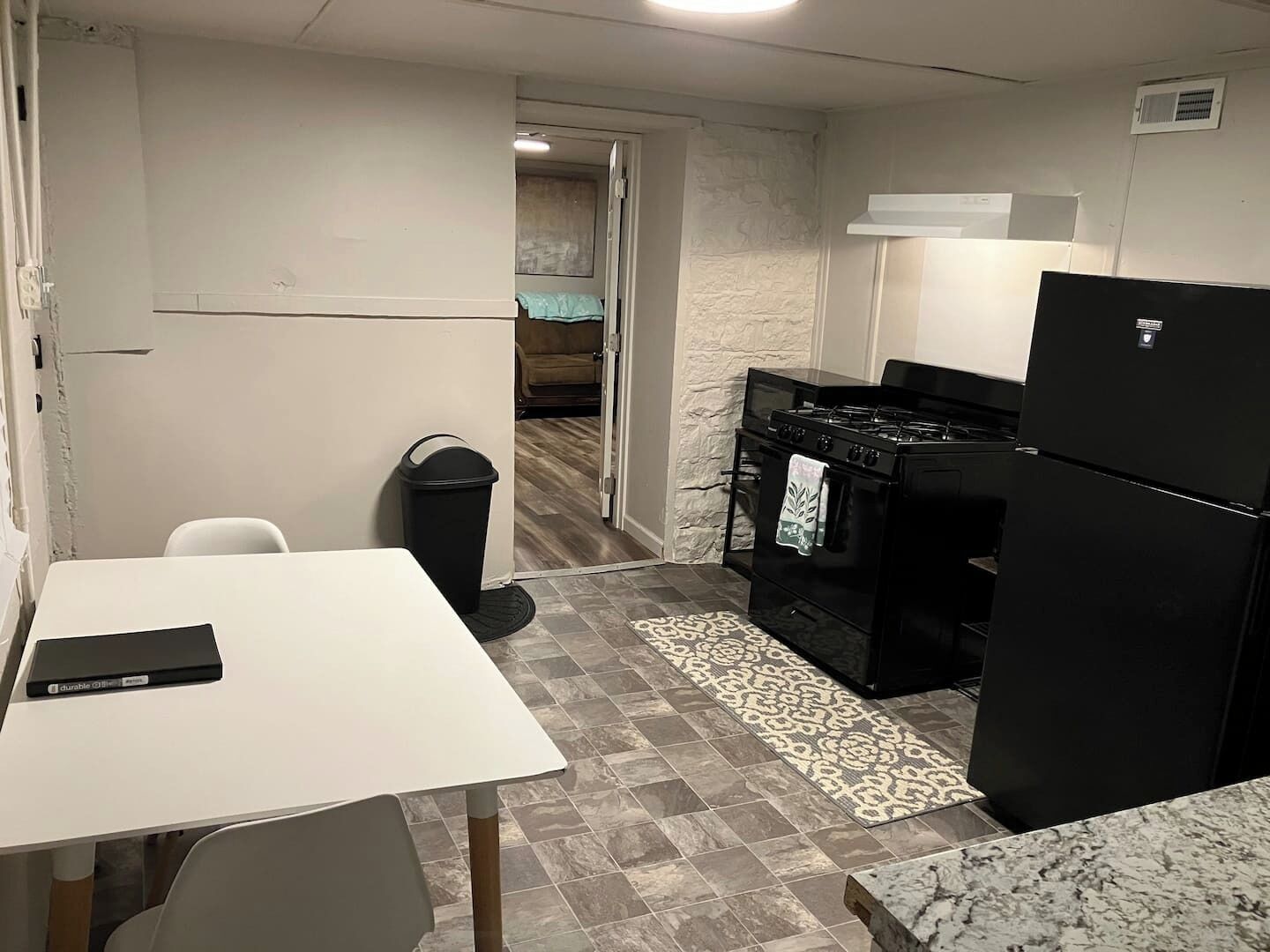 A compact kitchen with a white table, black appliances, and a patterned rug.