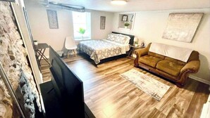 A bedroom with a bed, a brown sofa, a desk, and a chair.