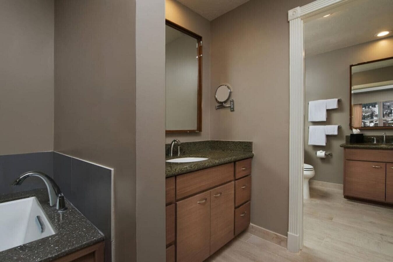 Un baño moderno con lavamanos de granito, muebles de madera, un espejo y un inodoro.