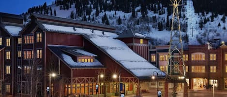 A hotel with a ski lift, snow-covered roofs, and a mountainous backdrop.