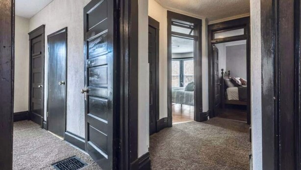 A hallway with three dark wooden doors leading to a bedroom with a bed and a nightstand. - Spacious five-bedroom home in the heart of Kansas City - Fast highway access (Kansas City)