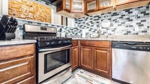 A kitchen with wooden cabinets, a stainless steel dishwasher, a black stove, and a tiled backsplash. - Spacious five-bedroom home in the heart of Kansas City - Fast highway access (Kansas City)