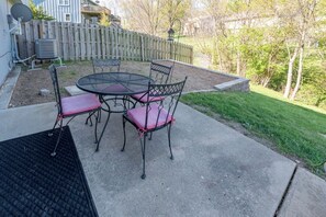 Eine Terrasse mit rundem Tisch und vier Stühlen, ein Holzzaun und eine Rasenfläche.