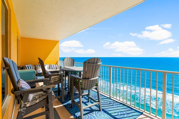 A balcony with a view of the ocean, featuring a table and chairs, a sofa, and a railing.