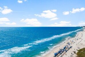 A beach with a row of blue umbrellas and sun loungers along the shoreline.