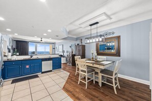 A modern kitchen with blue cabinets, a wooden dining table, and a large window.