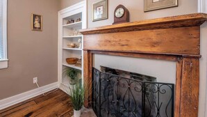 Une pièce avec une cheminée en bois, une étagère blanche ornée d’objets décoratifs et une plante en pot.