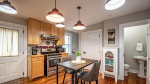 Une cuisine de taille réduite, dotée de meubles en bois, d’une cuisinière et de luminaires suspendus.