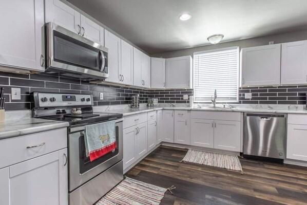 A modern kitchen with white cabinets, a stainless steel range, a microwave, and a dishwasher.