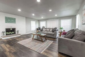A modern living room with a fireplace, grey sofas, and a patterned rug.